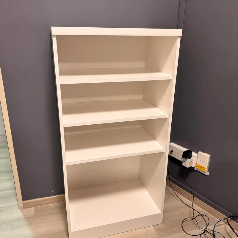 White open bookshelf with three adjustable shelves standing against a grey bedroom wall